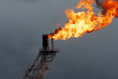 Eine große Flamme brennt an der Spitze einer industriellen Gasfackel vor einem dunklen, bewölkten Himmel und setzt Feuer in die Luft frei.