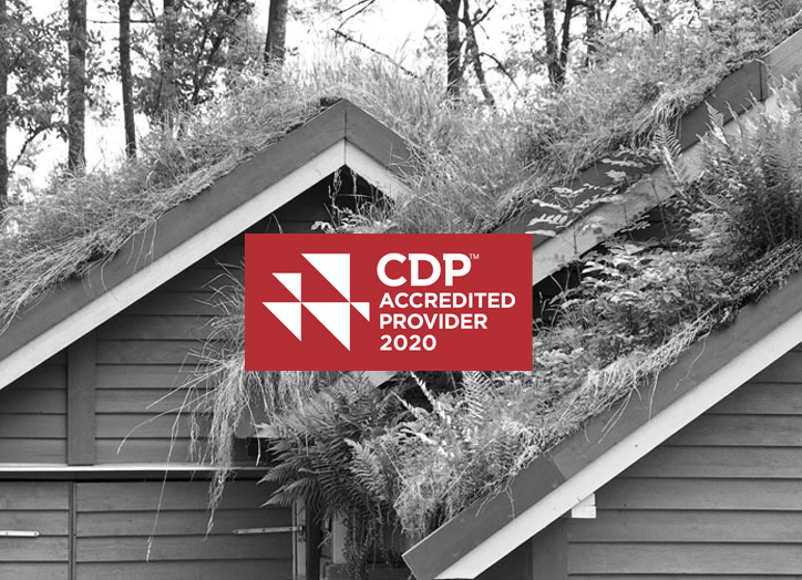 Ein Haus mit einem grünen Dach, das mit Gras und Pflanzen bedeckt ist; in der Mitte ein rotes Abzeichen mit der Aufschrift CDP Accredited Provider 2020 in weißer Schrift. Im Hintergrund sind Bäume zu sehen.