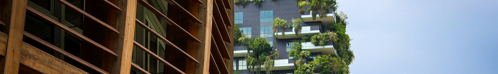 Corporate-Carbon-Footprint_Wide A modern high-rise with balconies covered in greenery is visible beside a wooden building structure, set against a clear blue sky.