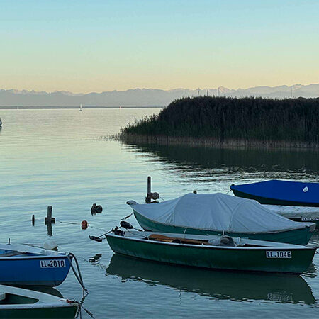 Auf einem ruhigen See, mit Bergen im Hintergrund und unter einem klaren Himmel, lagen mehrere kleine Boote vor Anker.